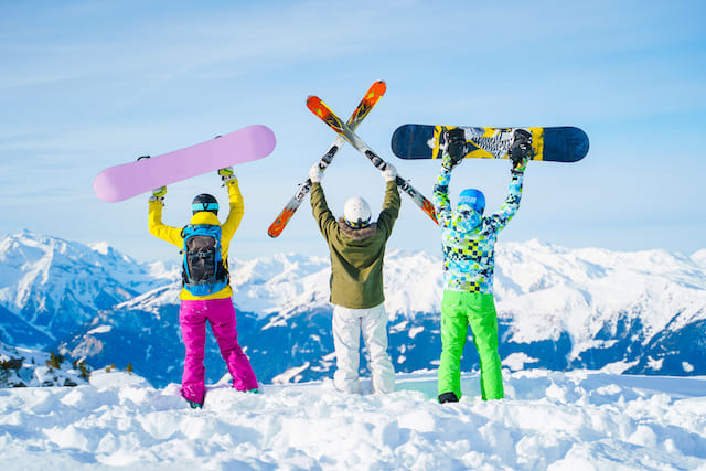 雪山でスキー板とスノーボードを掲げている人たち