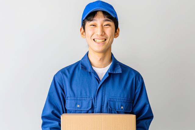 ダンボールを持った青い作業着の日本人男性